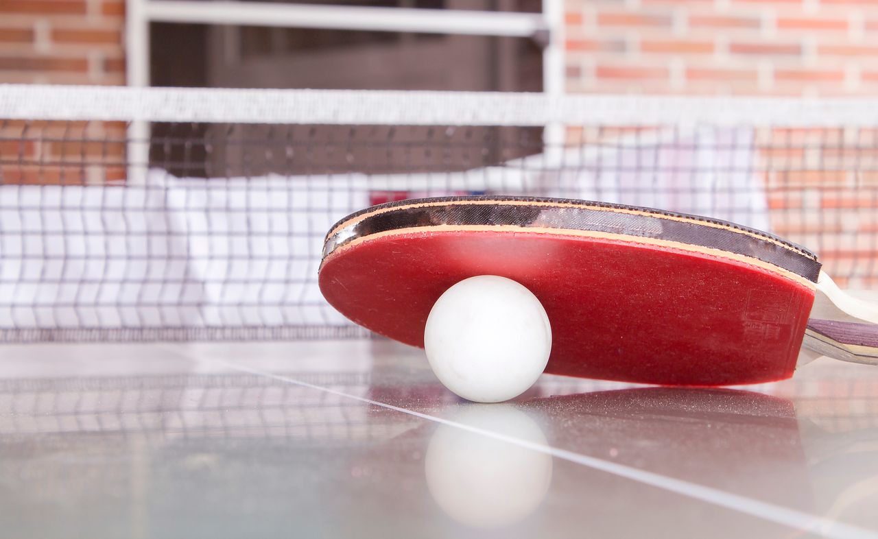 heros-img Close-up shot of a table tennis paddle and ball on a table, capturing the essence of the sport.