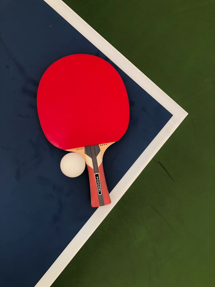 services-02 A red table tennis paddle and ball on a blue and green table surface.