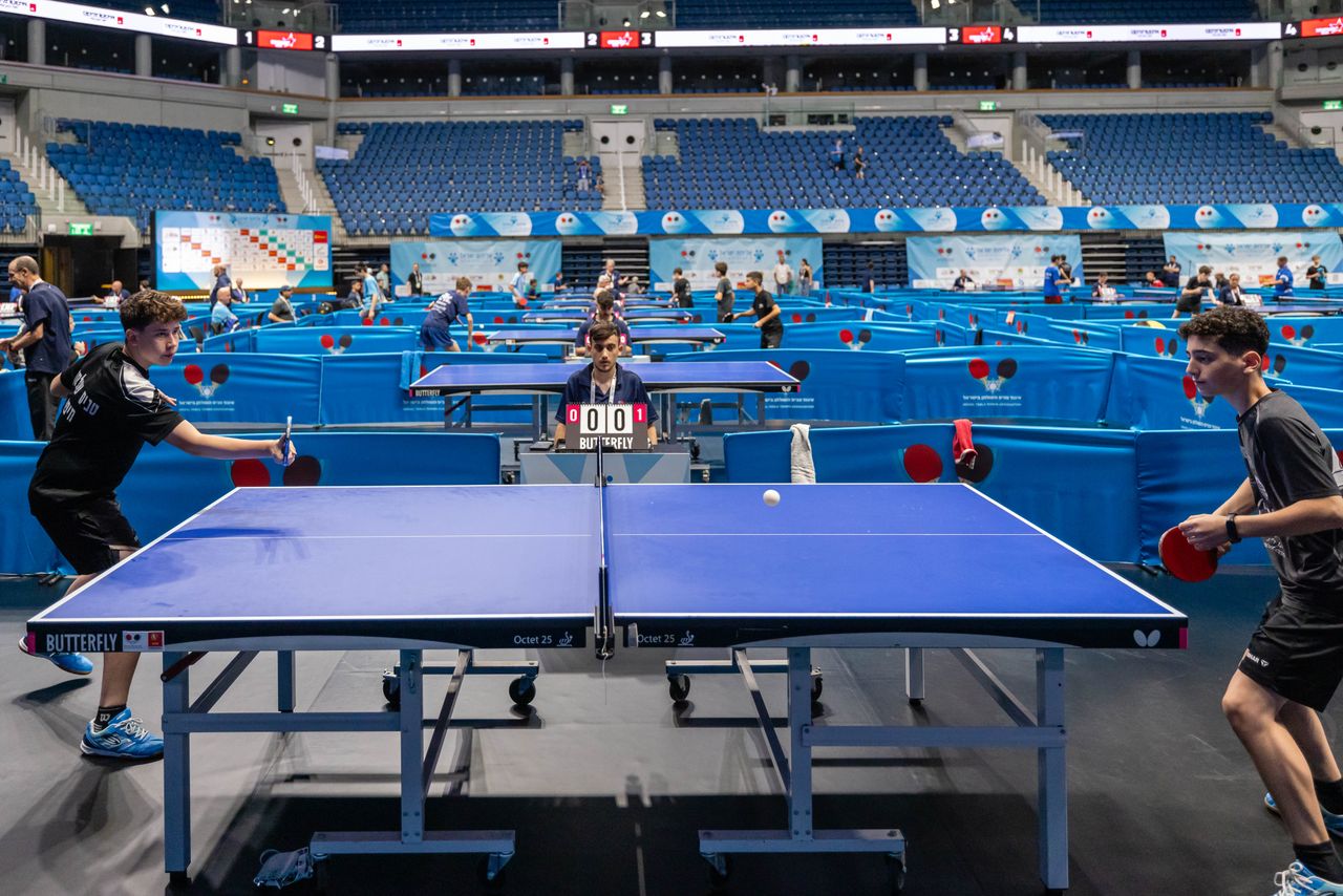 who-we-are Players compete in a lively table tennis tournament in a large indoor stadium.