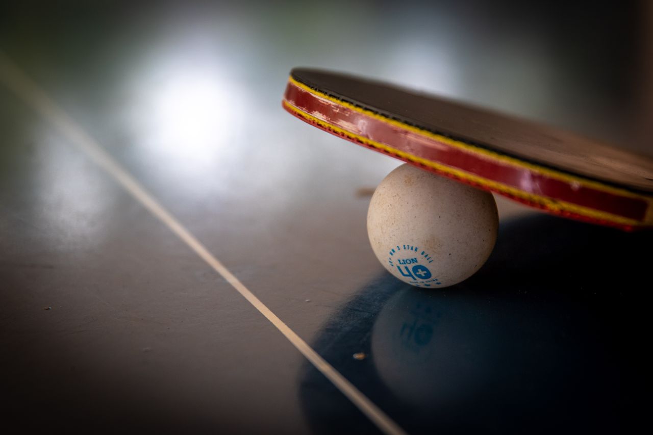 services-03 Close-up of a table tennis racket balancing on a ball indoors, emphasizing balance and sport.