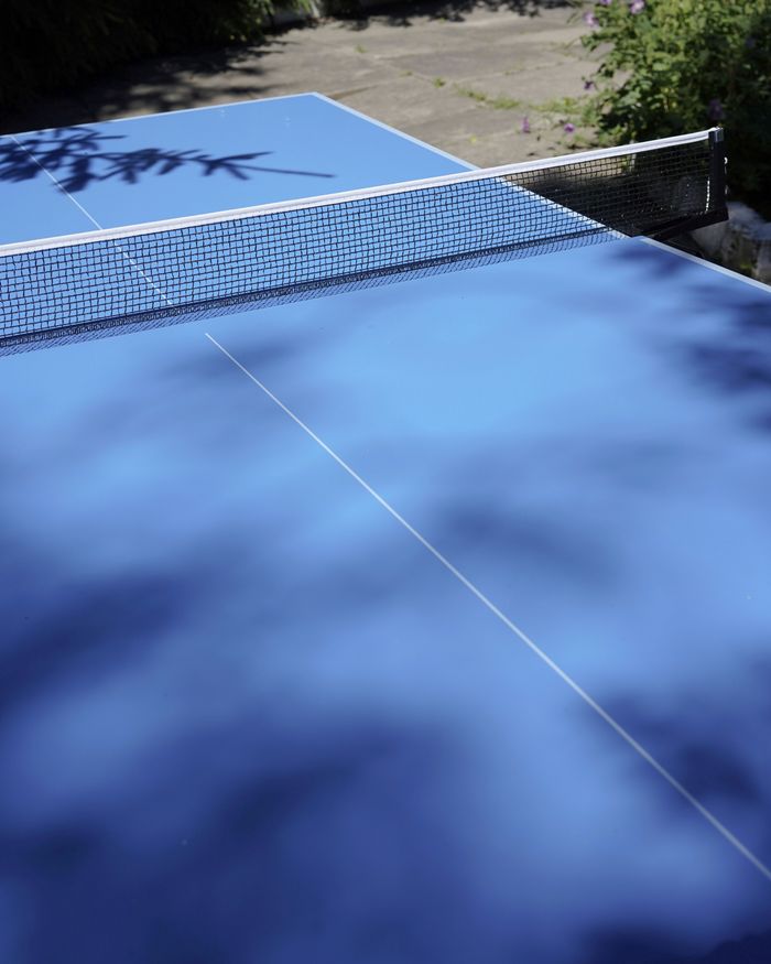 about-us Close-up of a blue ping pong table and net under clear daylight outdoors.